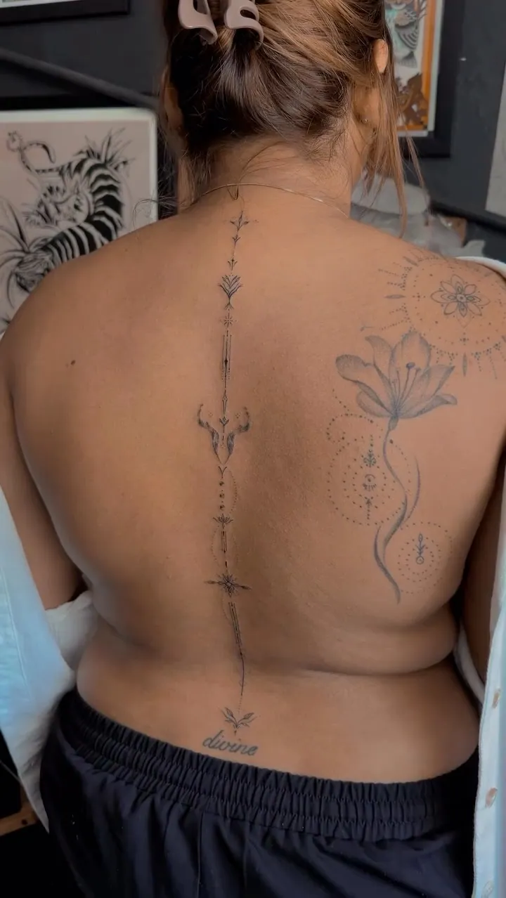 An ornamental fineline piece following the line of the spine, balanced left to right, ending in a small motif at the lower back.